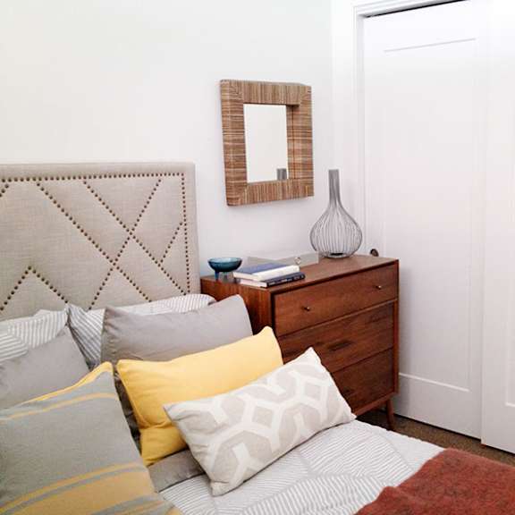 a bedroom with a bed, pillows, a dresser, and a mirror.